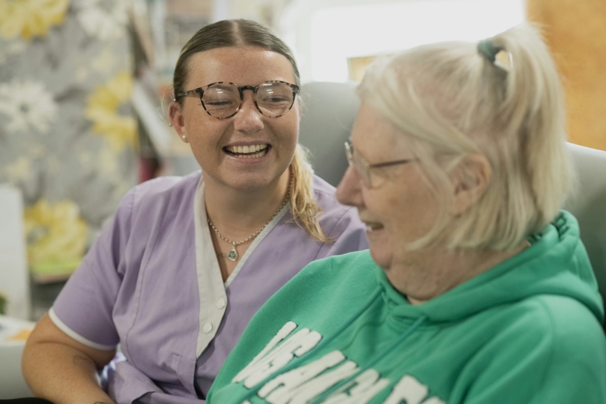 Herzliche Betreuung: Pflegekraft und Seniorin lachen gemeinsam