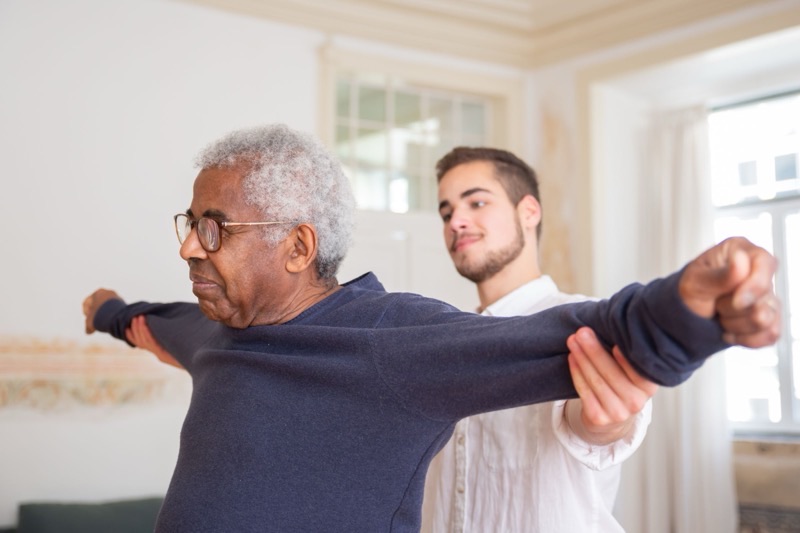 Pflegekraft unterstützt einen Senior bei Bewegungsübungen